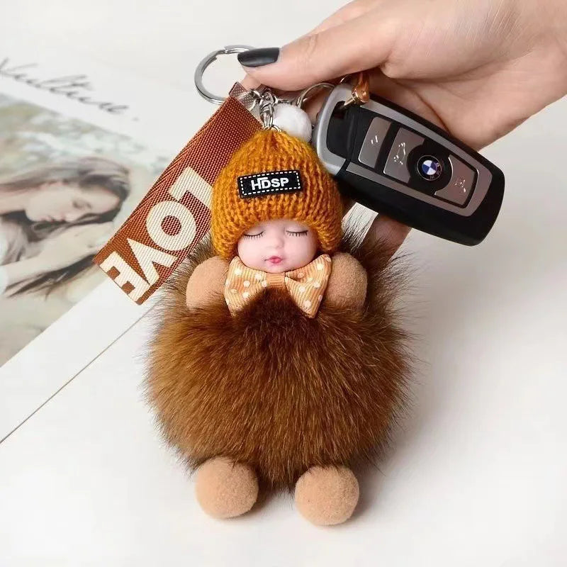 A fluffy brown plush doll with a blonde face and bow is attached to a keychain featuring an HDSP device.