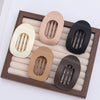 A set of five flat circular hair clips in various neutral tones displayed in a wooden tray.