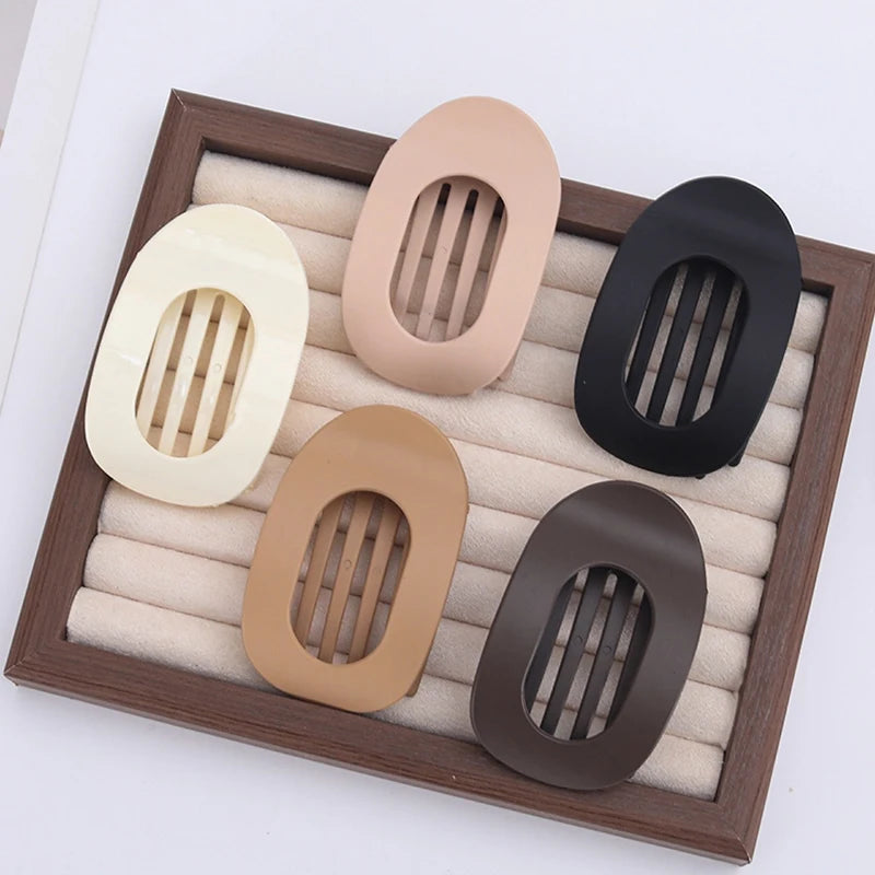 A set of five flat circular hair clips in various neutral tones displayed in a wooden tray.
