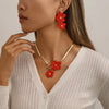 A close-up of a woman wearing a gold floral pendant necklace and matching earrings against a light sweater.