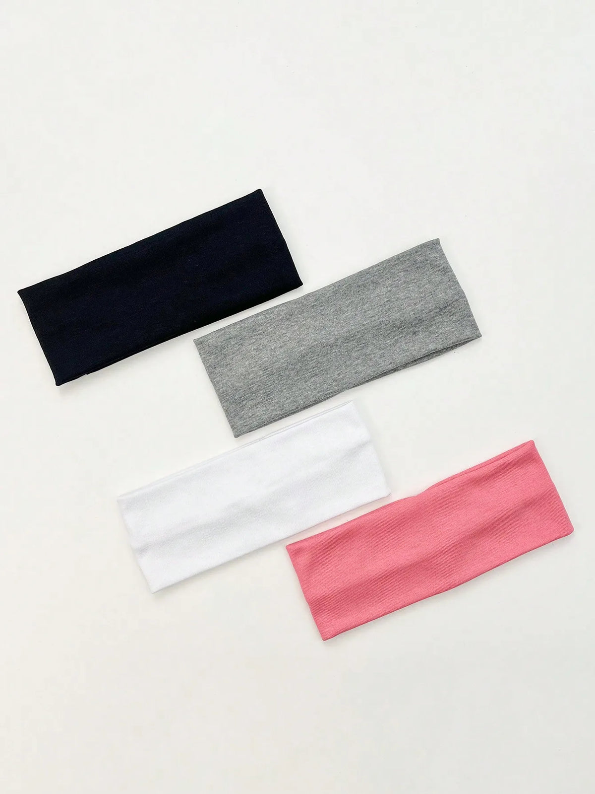 A set of four knitted hair bands in navy blue, gray, white, and pink laid diagonally on a light background.