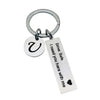 Silver keychain with a circular charm featuring a stylized initial and a tag that reads I need you here with me