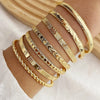 A stack of gold geometric minimalist bracelets worn on a wrist.