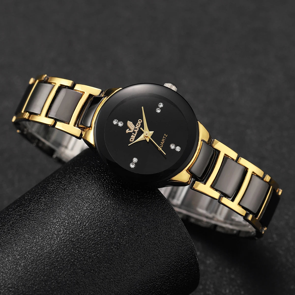 A black and gold couple's analog quartz watch set resting on a dark surface.