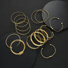 A collection of gold geometric stackable minimalist bracelets arranged on a dark surface.