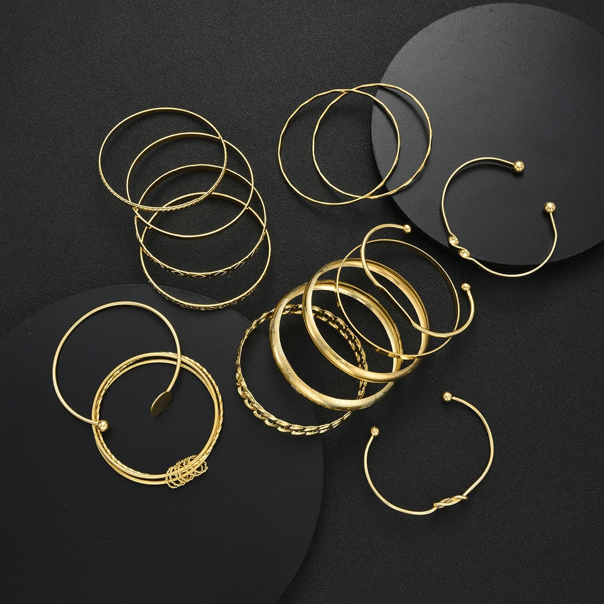 A collection of gold geometric stackable minimalist bracelets arranged on a dark surface.