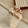 A close-up of a gold quartz fashion wristwatch worn on a hand, resting on a beige fabric and wooden frame.