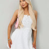 A blonde woman models a white floral lace dress and matching headscarf set.