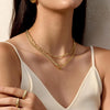 A close-up of a gold layered Cuban link necklace worn around the neck against a light-colored top.