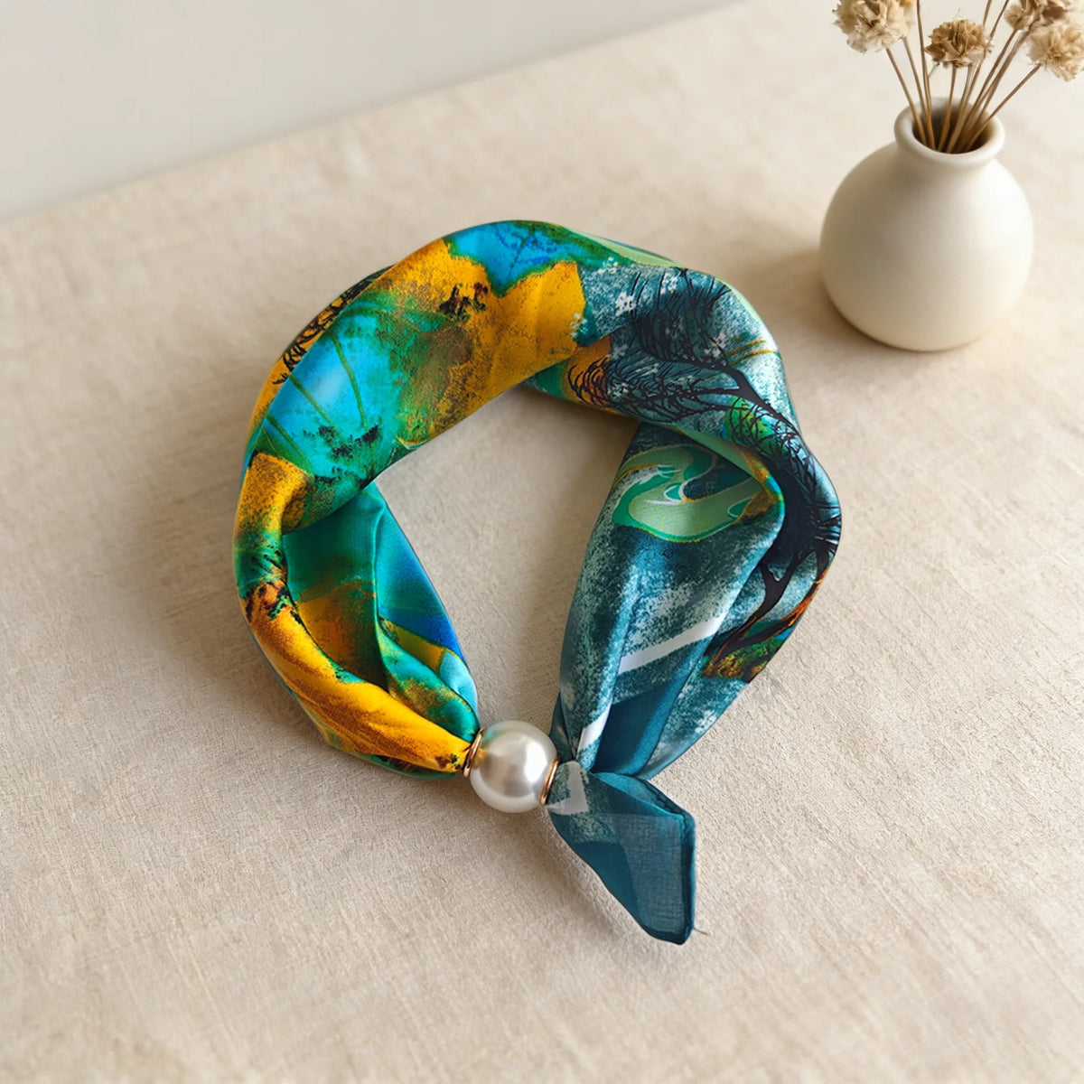 A silk scarf featuring a vibrant blue and yellow abstract print tied with a fabric bow and finished with a pearl bead.