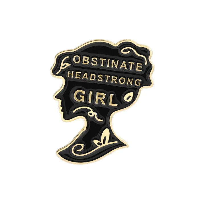 A black enamel lapel pin featuring the text OBSTINATE HEADSTRONG GIRL in gold lettering.