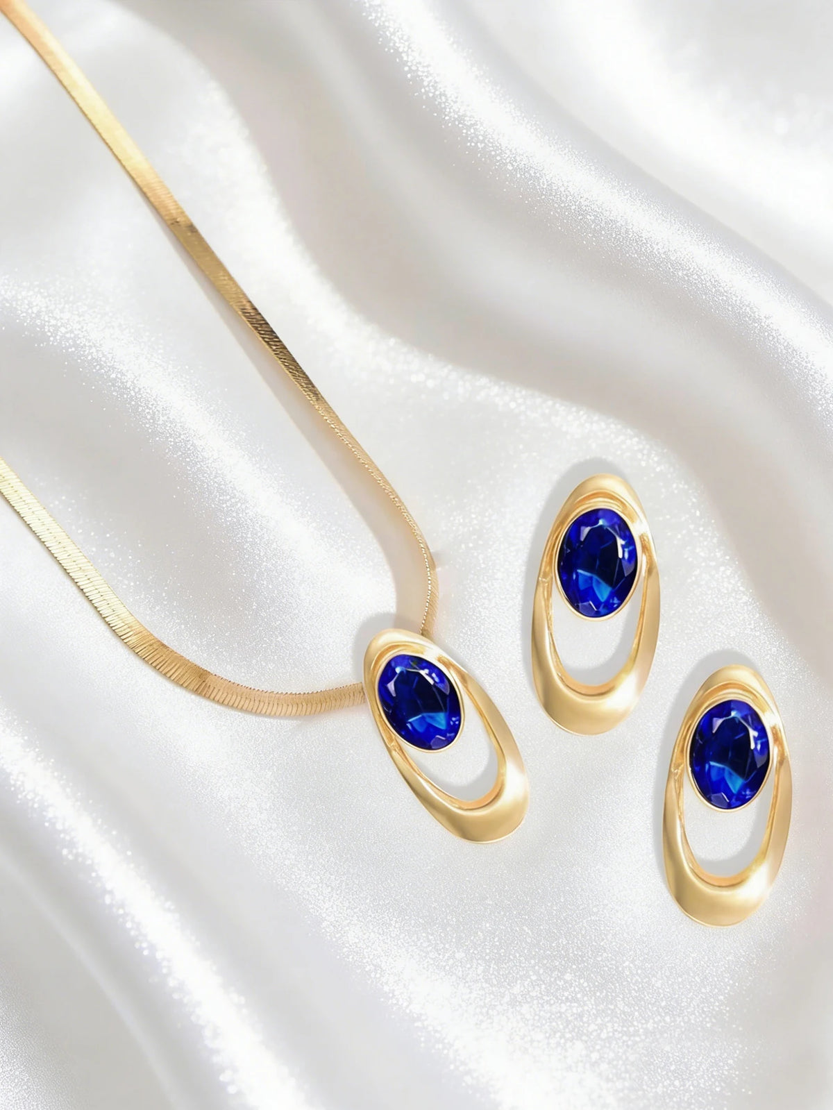 Gold and blue oval three-ring buckle necklace set displayed on a white satin fabric.