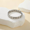 A silver stainless steel charm bracelet is displayed on a white stone surface.