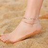Gold plated initial letter anklets worn on a foot in the sand