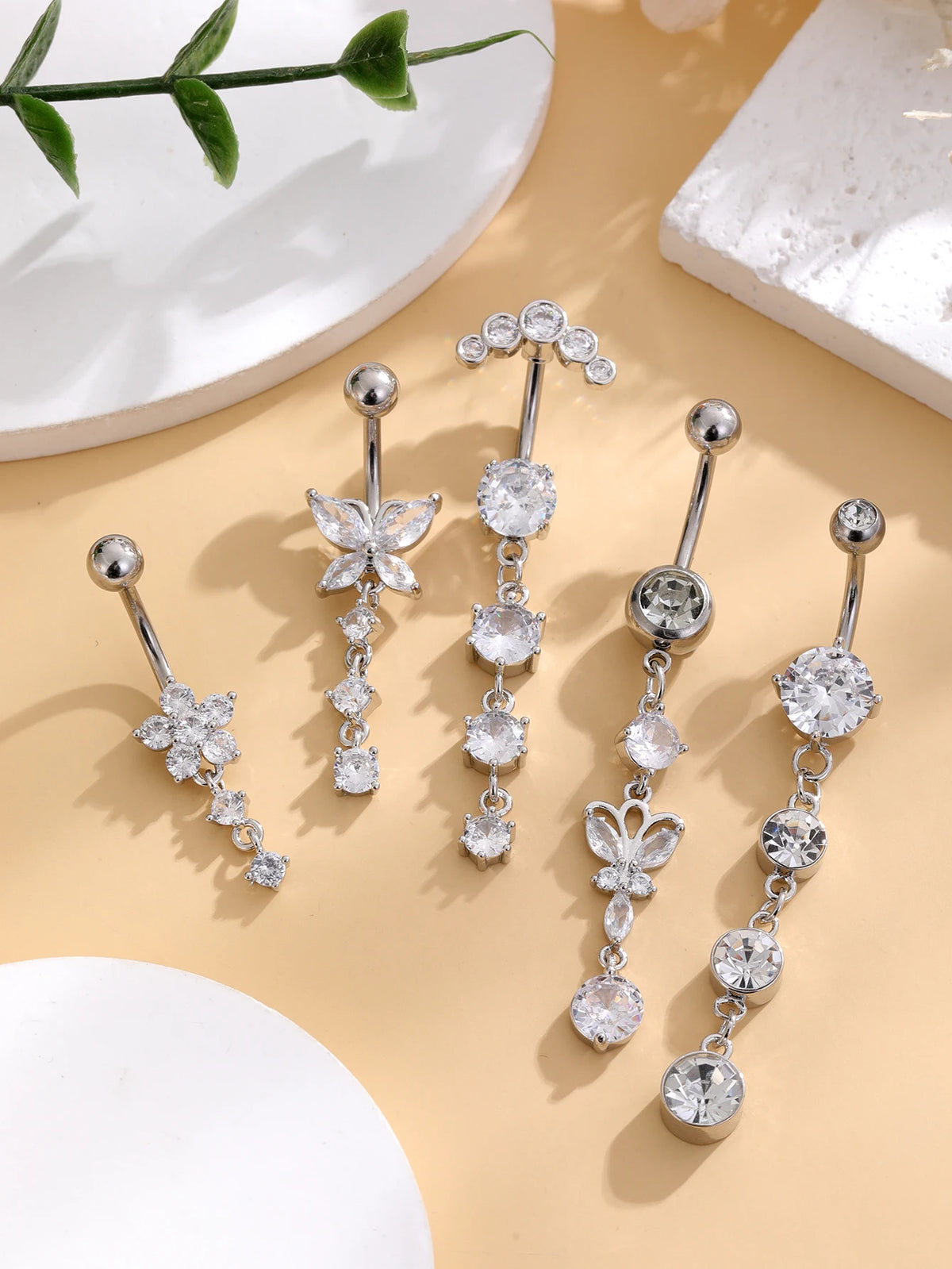 A set of five gold stainless steel dangled belly button rings featuring floral and round diamond-cut stones.
