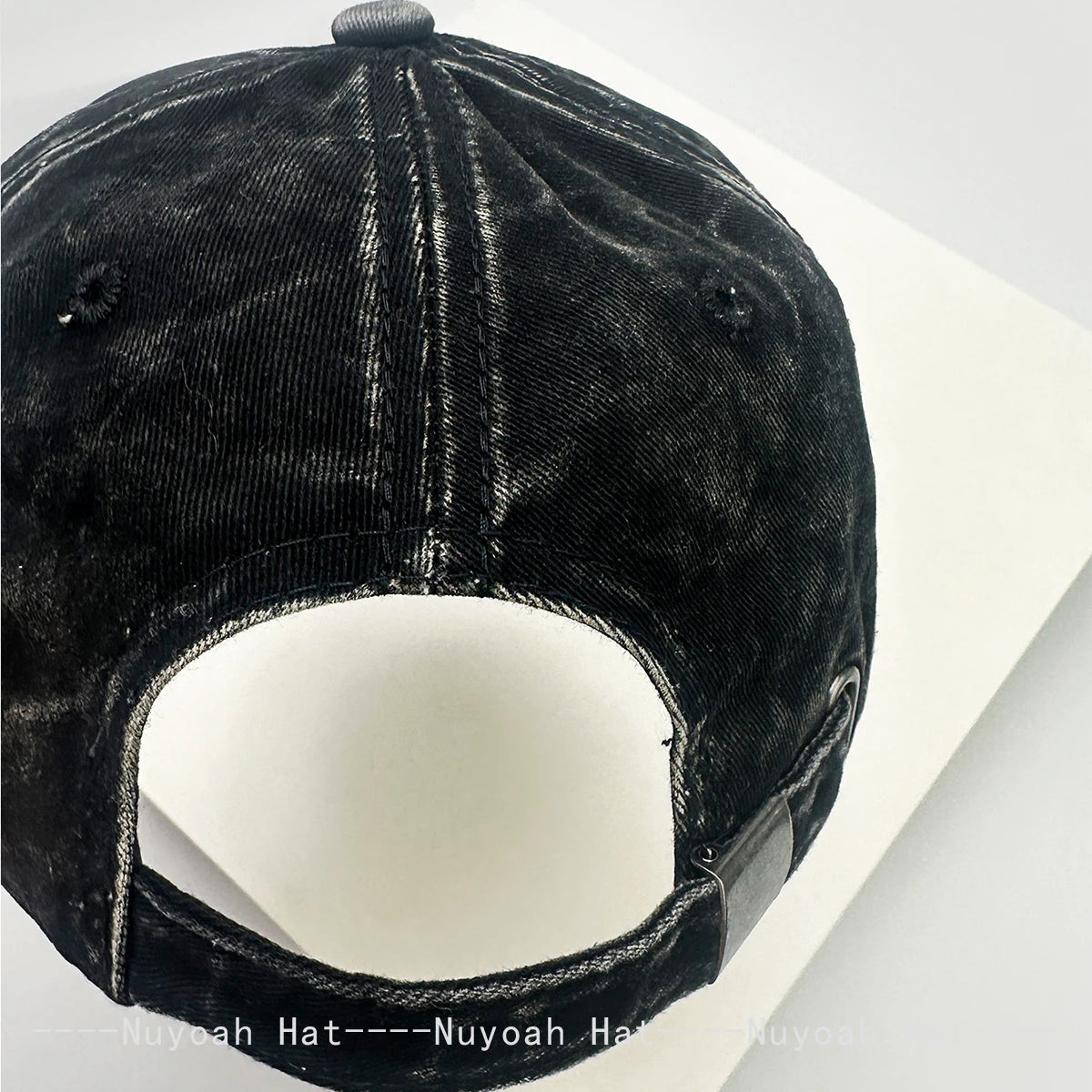 A close-up view of a black denim baseball cap with a mesh back and embroidered lettering.