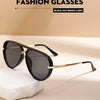 Une paire de lunettes de soleil noires avec une monture métallique dorée posées sur une surface blanche.