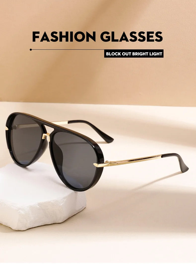 Une paire de lunettes de soleil noires avec une monture métallique dorée posées sur une surface blanche.