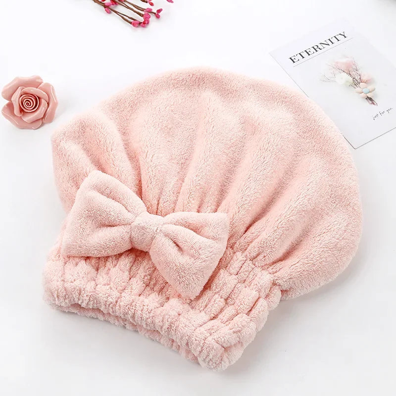 A soft pink microfiber hair drying towel with a pom-pom detail is displayed on a white surface.
