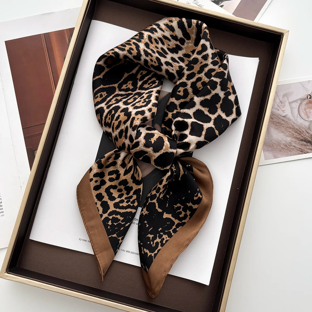 A luxury leopard print silk scarf tied in a bow, displayed in a wooden frame.