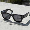 Black square sunglasses resting on a light gray concrete surface with a measurement line.