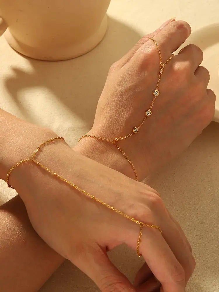 A close-up of a hand wearing a delicate gold-plated bracelet with small zircon stones.