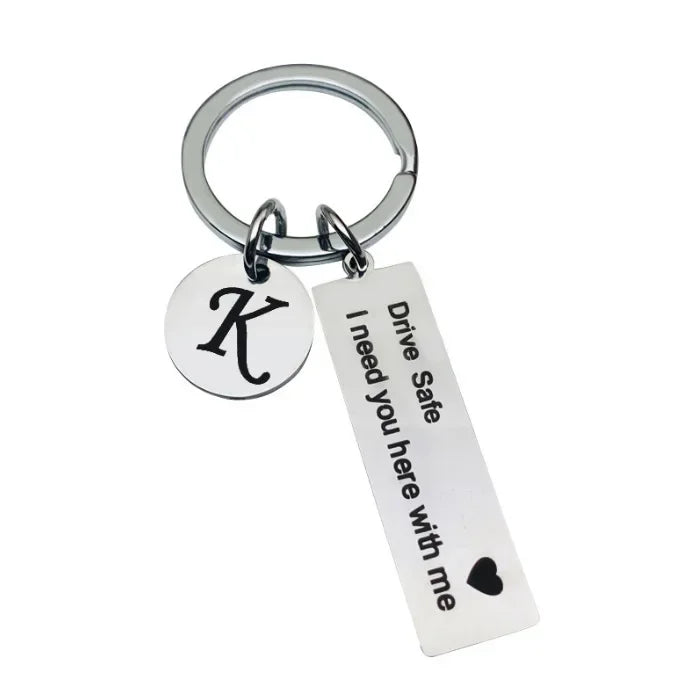 Silver keychain with a custom initial K and the message Drive Safe I need you here with me
