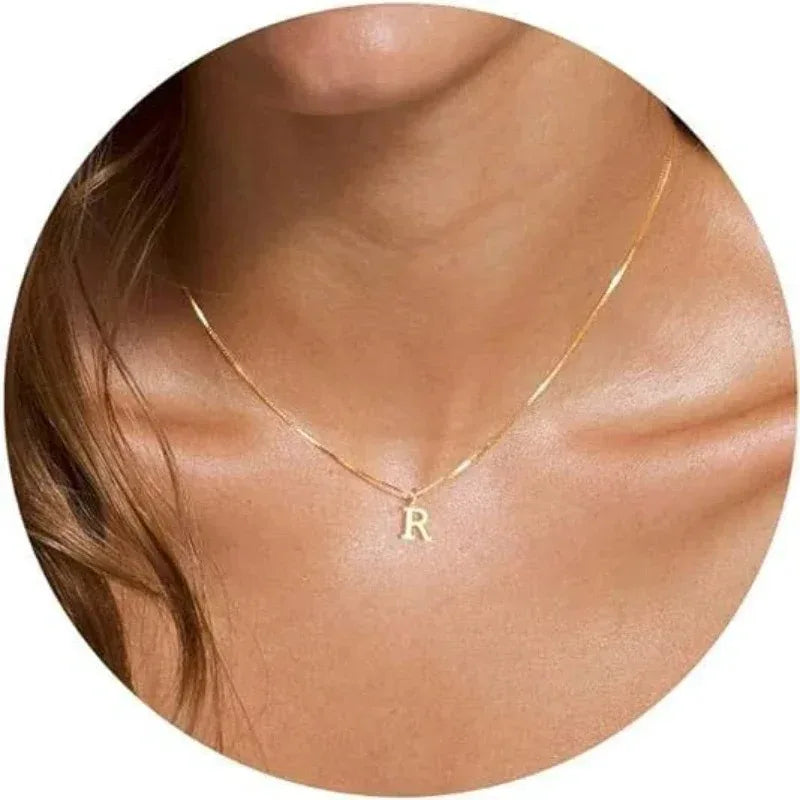 A close-up of a gold plated alphabet initial necklace with an R pendant worn around the neck against skin.