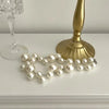 A strand of elegant simulated pearl choker necklace rests on a white surface next to a gold-toned candlestick.