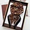 A luxury leopard print silk scarf is displayed in a wooden box on white paper.