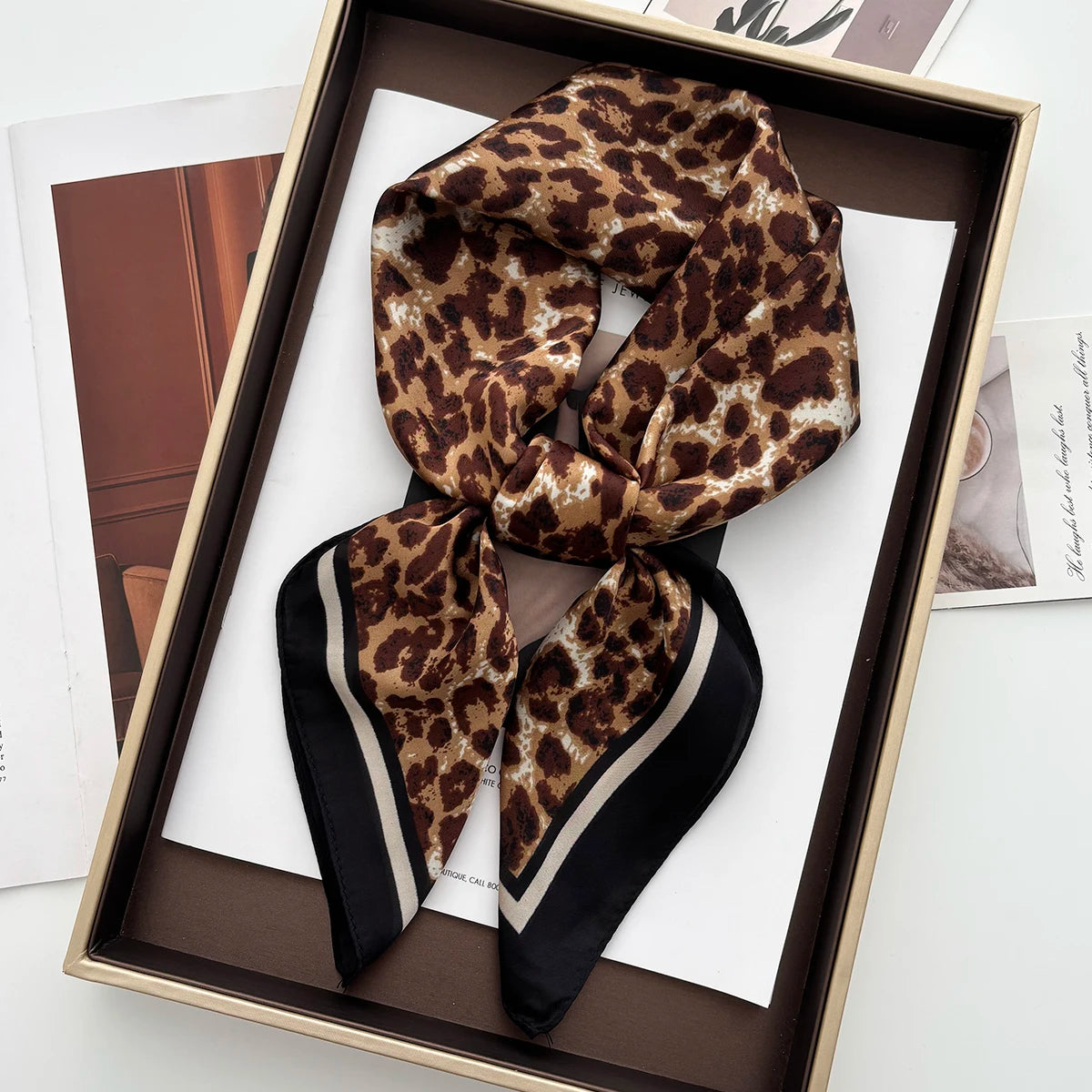 A luxury leopard print silk scarf is displayed in a wooden box on white paper.