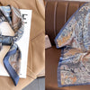 A silky scarf with a floral print in blue and gold tones is displayed next to a tan blazer.