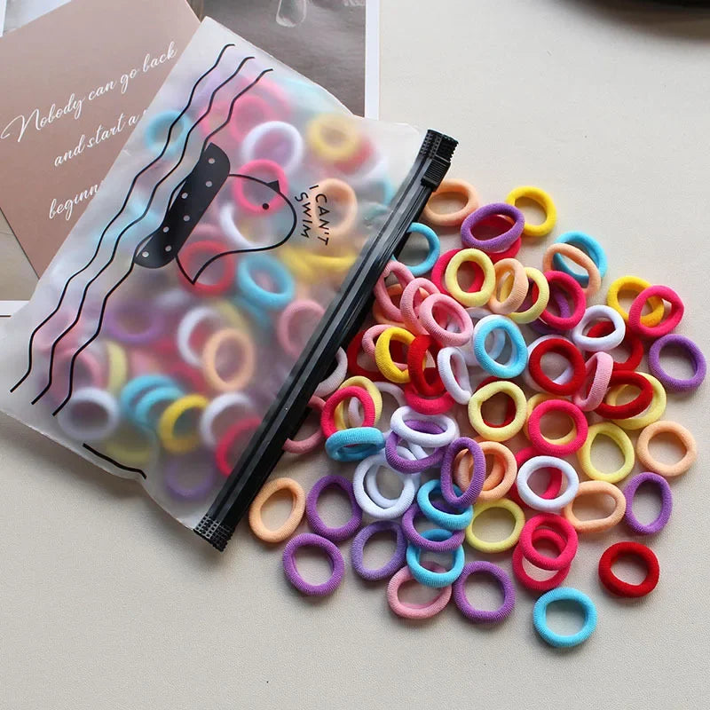 A pile of colorful elastic hair bands in various colors like pink, yellow, blue, and purple are shown next to a black applica