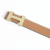 A tan leather dress belt with a brass buckle and stitching, shown diagonally.