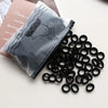 A black pouch of elastic hair bands is shown next to a pile of black, circular hair ties.