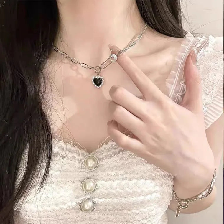 A close-up of a woman wearing a pink crystal heart necklace with a delicate chain and pearl accents.