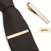 A close-up of a black textured tie with a gold metal tie clip attached.