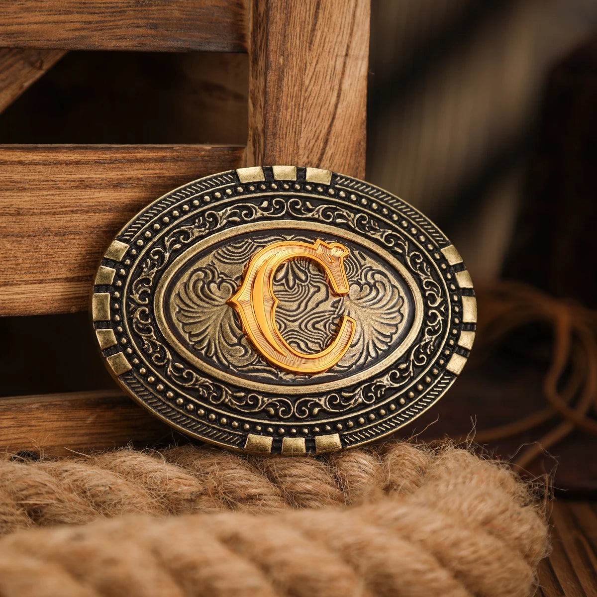 A vintage western belt buckle with an ornate gold design set in a dark metal frame, resting on a textured brown surface.
