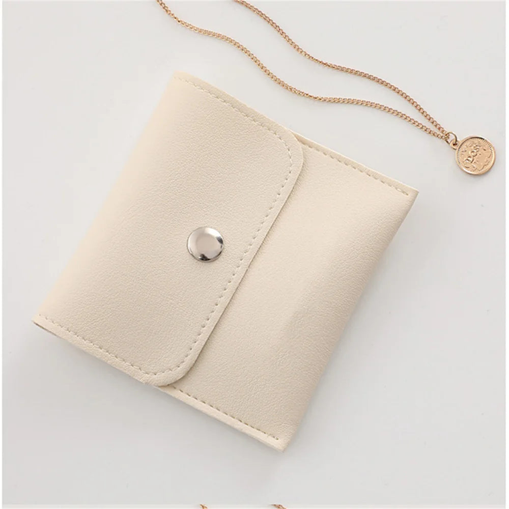 A beige PU leather jewelry pouch with a snap button and a gold chain attached.