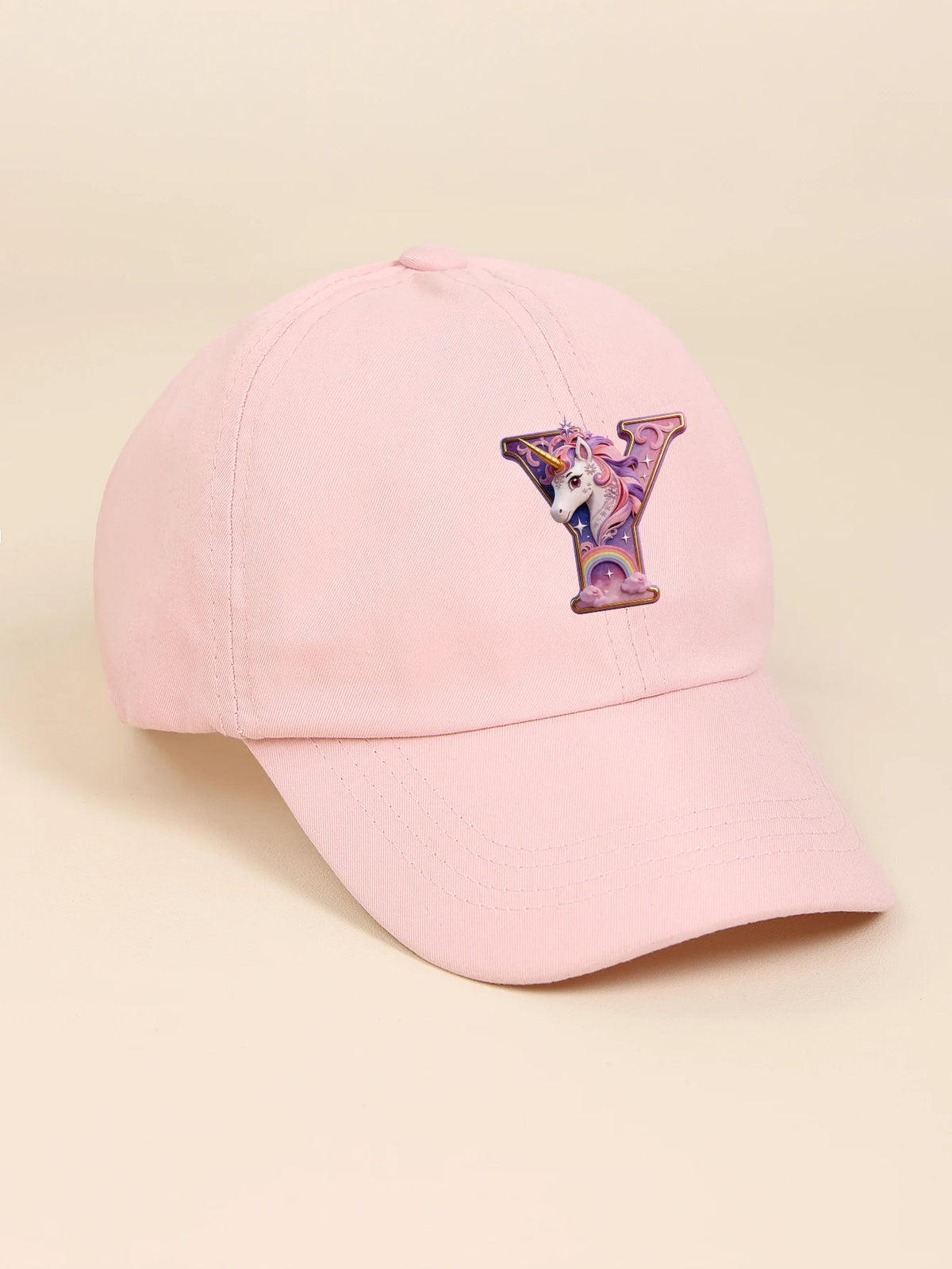 A pink baseball cap featuring a purple unicorn letter embroidered on the front.