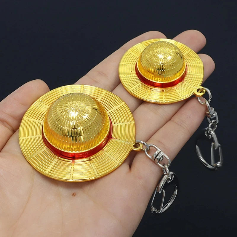 A golden anime style straw hat metal keychain is shown resting in a person's hand.