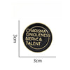 A round black lapel pin with gold lettering that reads Charisma Uniqueness Nerve & Talent