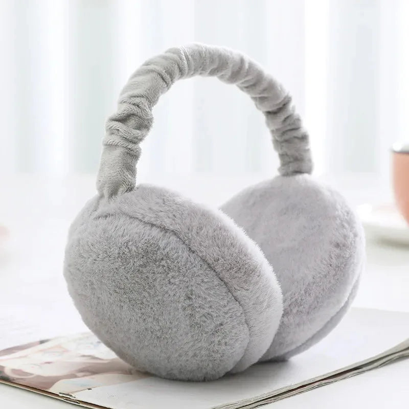 A pair of soft gray plush fur ear warmers or earmuffs resting on a white surface.
