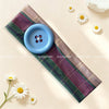 A purple and green plaid fabric headband with a blue button detail is displayed on a light background.
