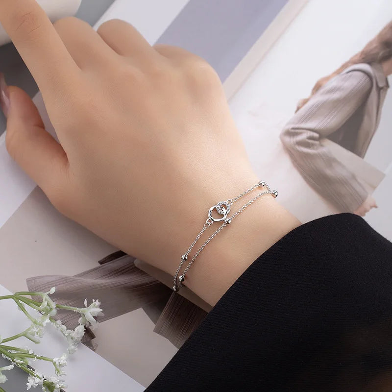 A close-up of a sterling silver double heart charm bracelet worn on a wrist against a light background.