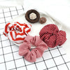 A set of three colorful knitted hair scrunchie headbands in red and white patterns are displayed on a white plate.