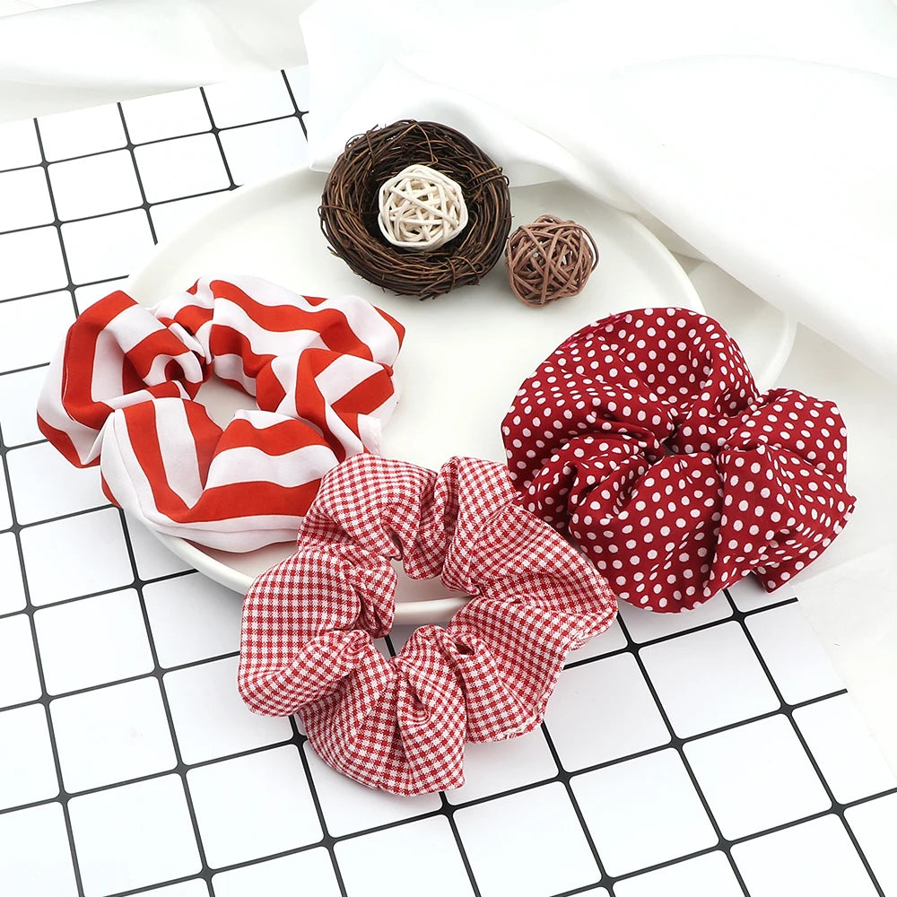 A set of three colorful knitted hair scrunchie headbands in red and white patterns are displayed on a white plate.