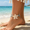 A woman wearing a white starfish anklet on her foot while standing on a sandy beach near the ocean.