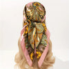 A silk scarf featuring an ornate gold and green paisley pattern tied around a blonde hairstyle.