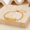 Gold stainless steel zodiac constellation charm bracelet spelling out TAURUS resting on a light beige surface.